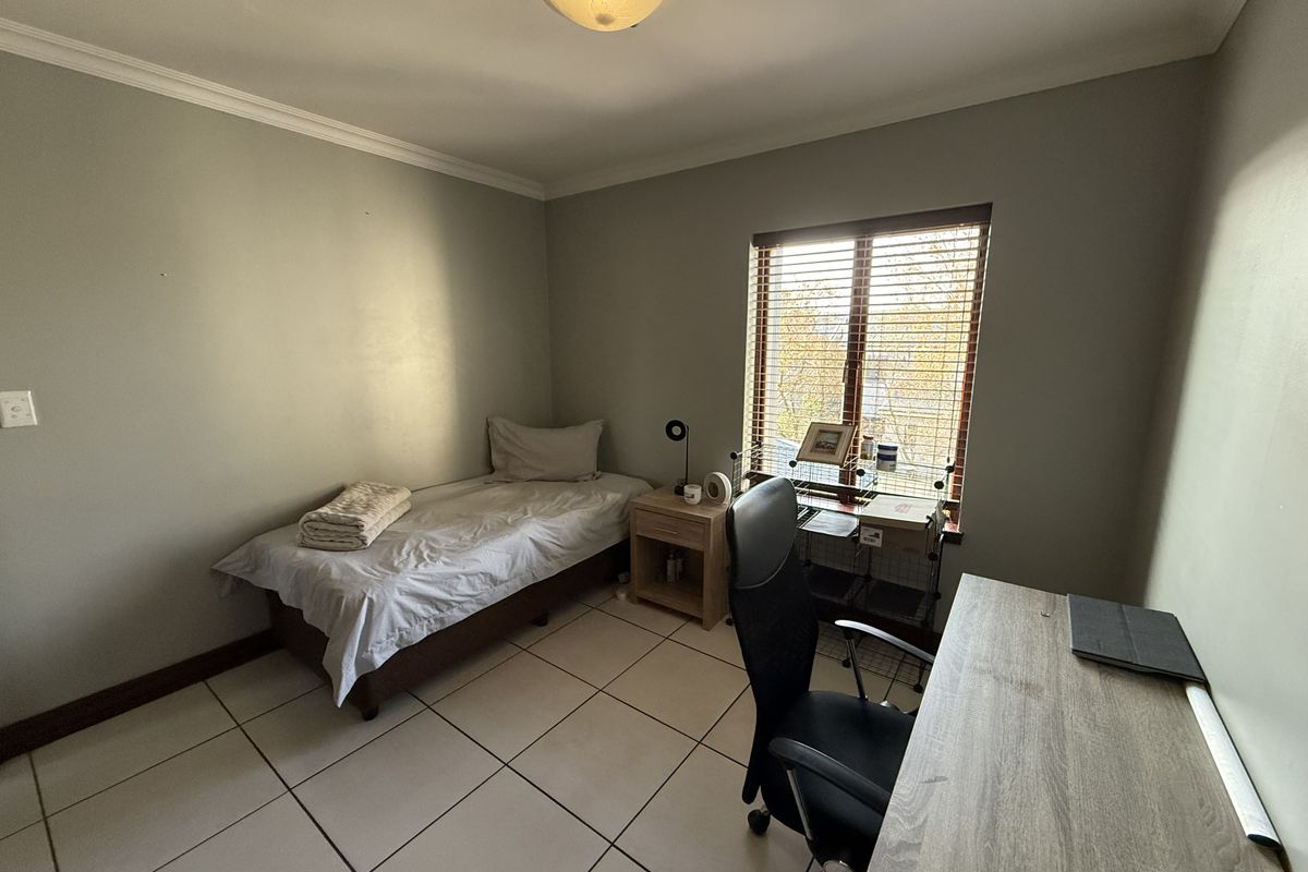 A functional bedroom featuring tiled flooring, neutral wall tones, and a window fitted with venetian blinds, providing a simple and practical living space.