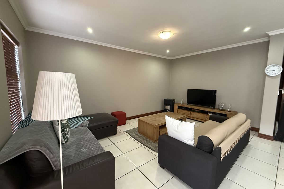 A spacious living room featuring neutral wall tones, tiled flooring, and recessed downlighting, providing a comfortable and well-maintained area for relaxation.