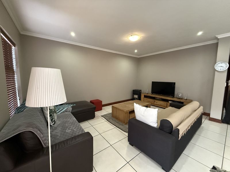 A spacious living room featuring neutral wall tones, tiled flooring, and recessed downlighting, providing a comfortable and well-maintained area for relaxation.