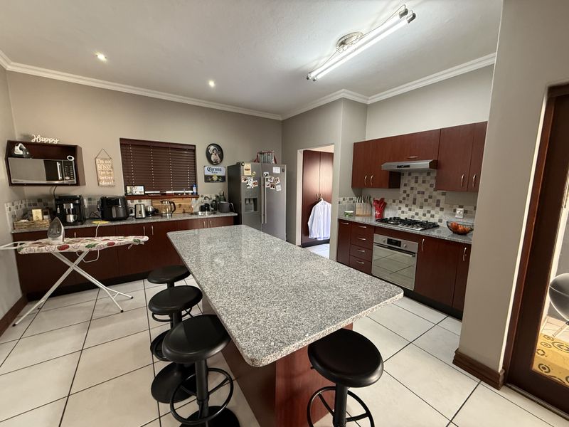 Spacious kitchen featuring dark wood cabinetry, granite countertops, a central island, and built-in appliances, complemented by neutral tiled flooring.