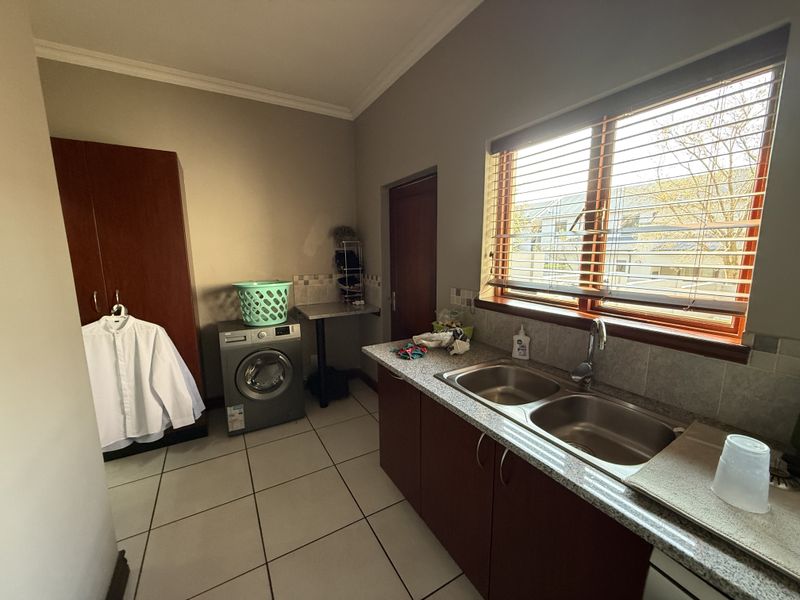 A functional laundry room featuring tiled flooring, granite countertops, a double stainless steel sink, and built-in cabinetry with ample storage space.