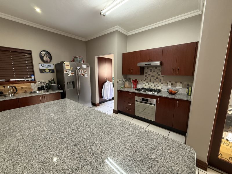 A functional kitchen featuring granite countertops, dark wood cabinetry, a built-in oven with gas hob, and a mosaic tile backsplash.