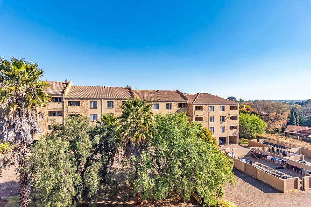 Aerial view of a multi-story apartment complex featuring brick exterior, tiled roofing, and a paved communal area with drying facilities.