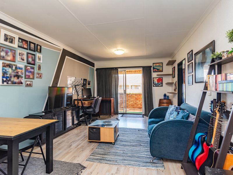 A well-lit living room featuring laminate flooring and a sliding glass door providing access to an outdoor balcony area.