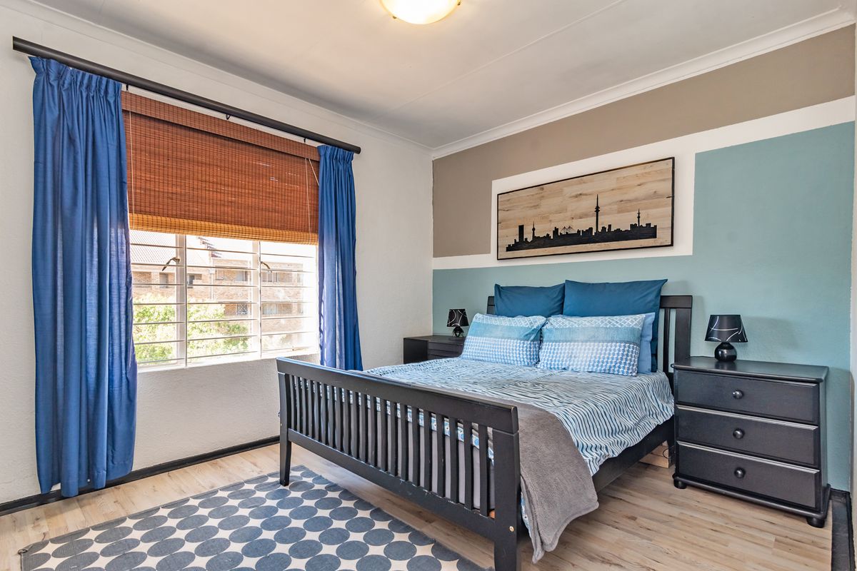 A well-maintained bedroom featuring laminate flooring, neutral wall tones with a feature accent wall, and a window fitted with security bars.