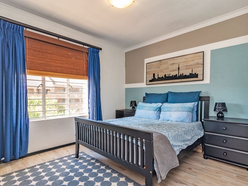 A well-maintained bedroom featuring laminate flooring, neutral wall tones with a feature accent wall, and a window fitted with security bars.