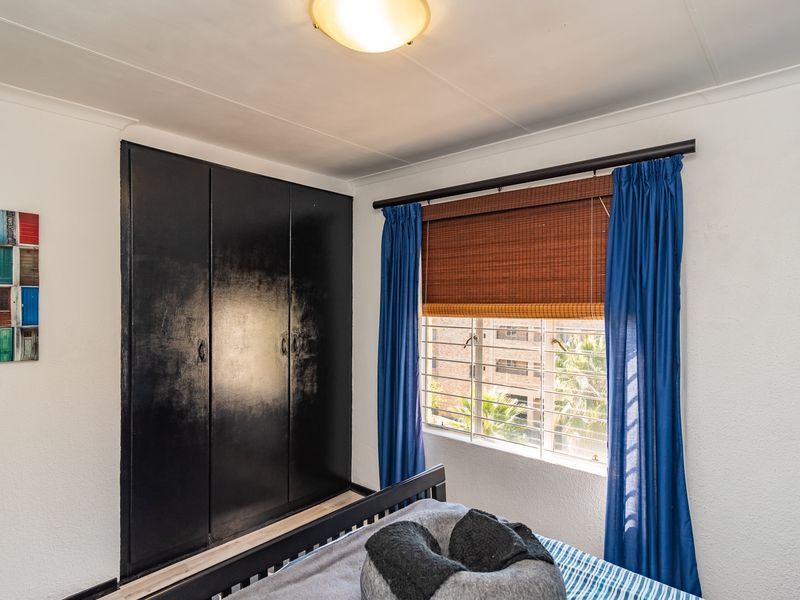 A bedroom featuring a built-in wardrobe with a dark finish, a window with security bars, and a central ceiling light fixture.