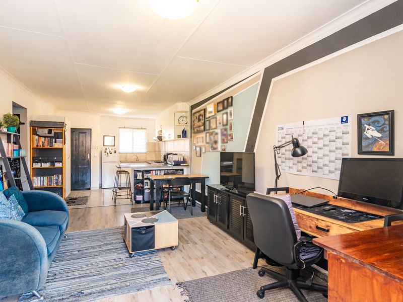 An open-plan living and kitchen area featuring laminate flooring, functional cabinetry, and a combined layout suitable for modern apartment living.