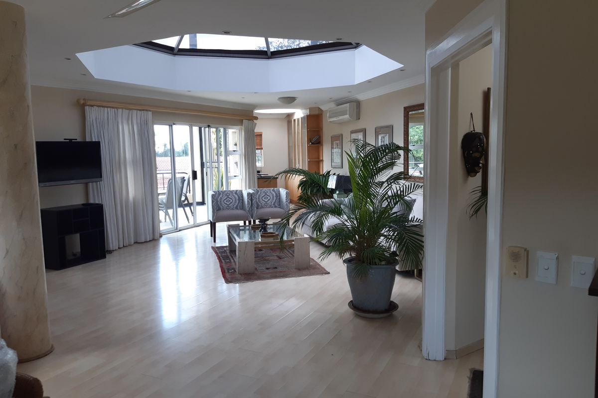 Spacious living room featuring a large central skylight, laminate flooring, air conditioning, and sliding glass doors leading to an outdoor area.