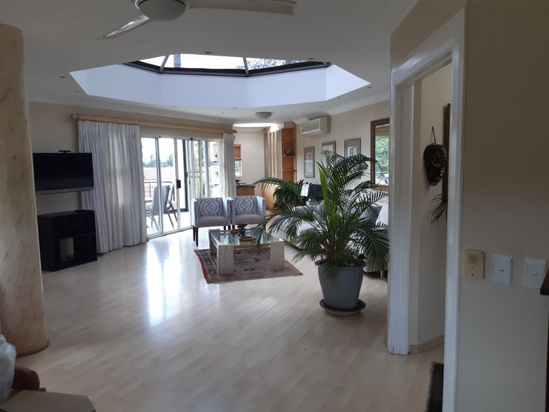 Spacious living room featuring a large central skylight, laminate flooring, air conditioning, and sliding glass doors leading to an outdoor area.