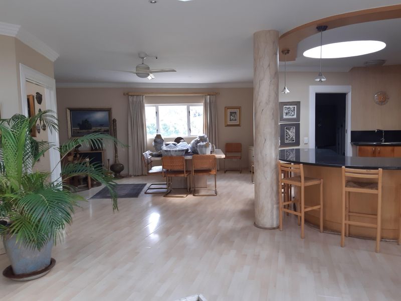 Spacious open-plan living and dining area featuring light laminate flooring, a curved breakfast bar with stone countertop, and integrated kitchen cabinetry.