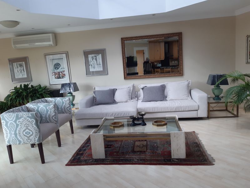 A spacious living room featuring a large skylight, recessed downlighting, and a wall-mounted split-system air conditioner, finished with light-toned laminate flooring.