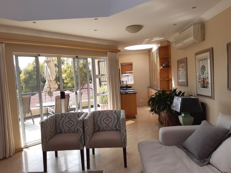 Bright open-plan living area featuring laminate flooring, recessed lighting, a skylight, and sliding glass doors leading to a balcony.