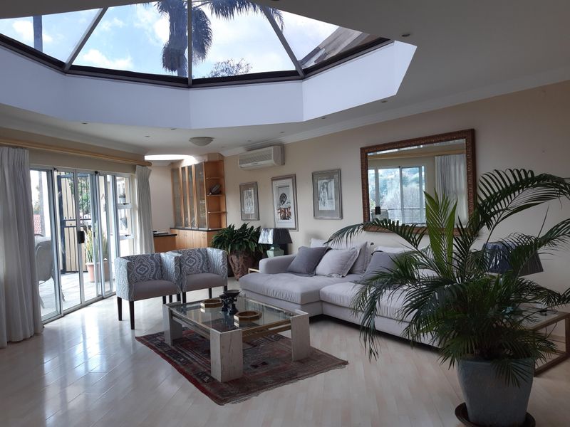 Spacious living room featuring a large architectural skylight, light wood-look flooring, and sliding glass doors leading to an outdoor area.