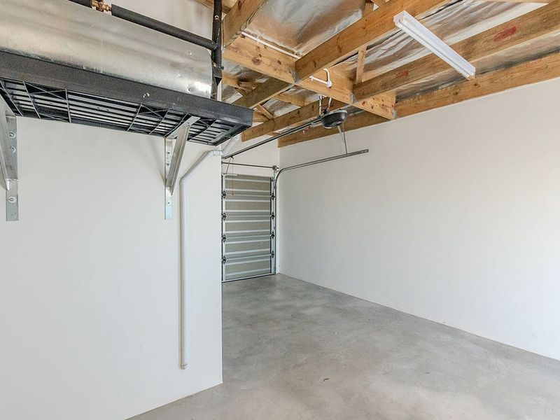A clean, empty garage space featuring exposed timber roof trusses, concrete flooring, and a functional sectional garage door.