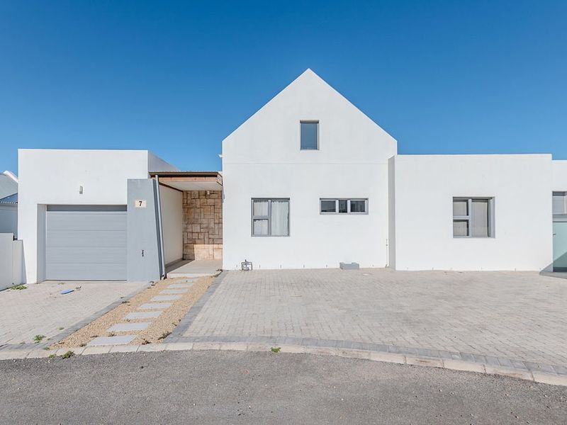 Modern single-story house featuring a clean white facade, stone-clad entrance, paved driveway, and an integrated garage.