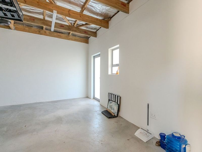 A spacious, empty garage featuring exposed timber roof trusses, concrete flooring, and functional lighting, offering a versatile utility or storage space.