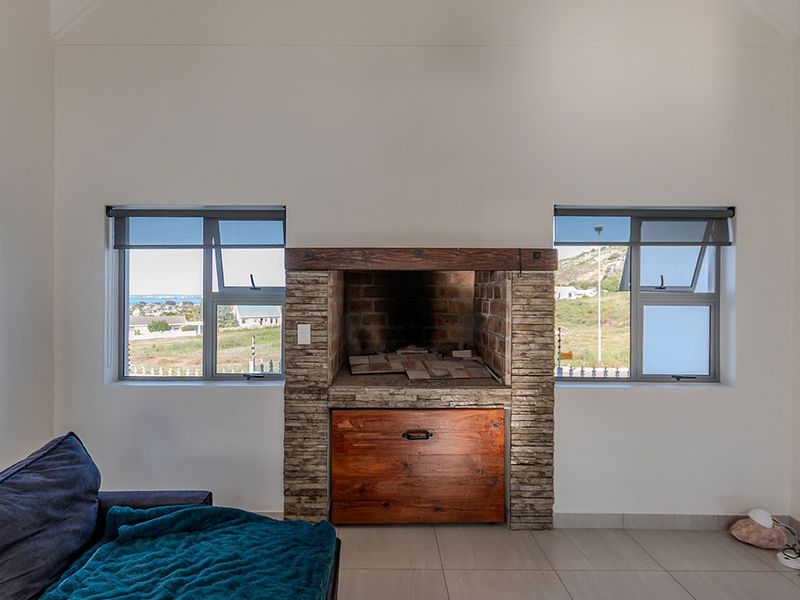 Living room featuring a prominent stone-clad built-in fireplace with a timber mantel, flanked by large windows with views and neutral tiled flooring.