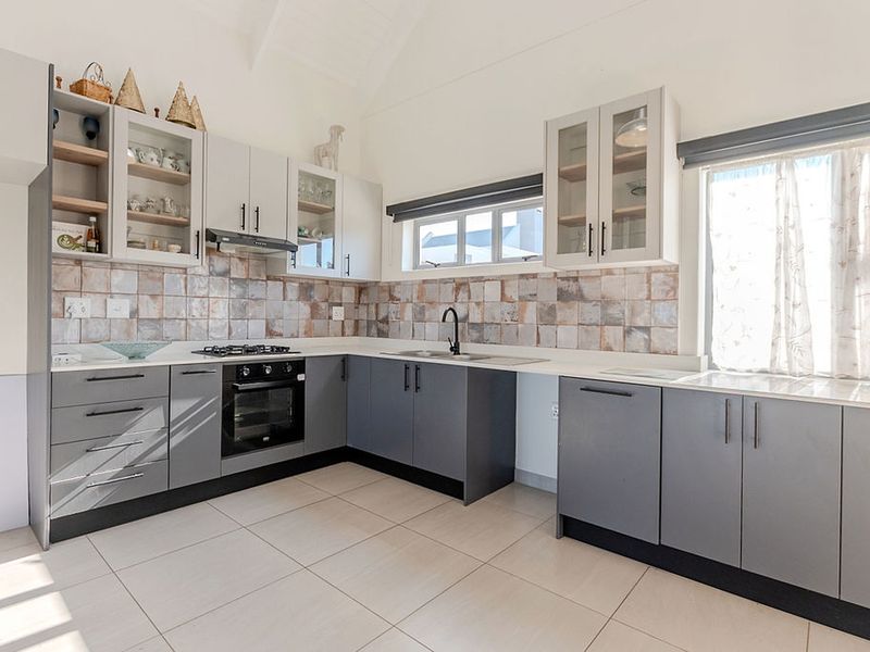Modern kitchen featuring grey cabinetry, a gas hob, built-in oven, tiled backsplash, and a vaulted ceiling, offering a clean and functional workspace.