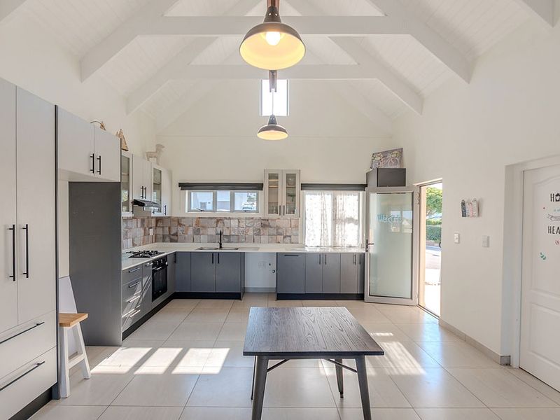 Modern kitchen featuring vaulted ceilings with exposed rafters, grey cabinetry, tiled backsplash, and integrated appliances, opening directly to the exterior.