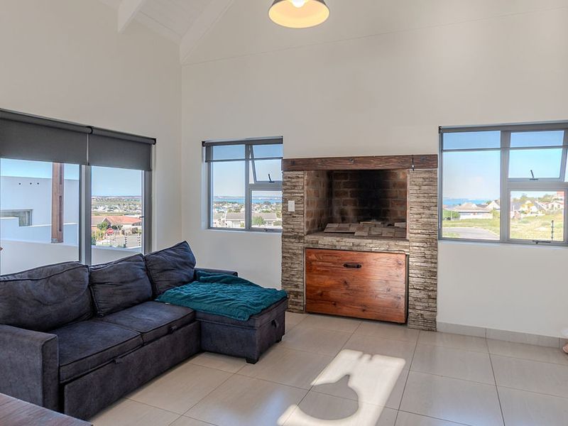 Bright living room featuring a built-in stone-clad fireplace, vaulted ceilings, tiled flooring, and large windows offering scenic coastal views.