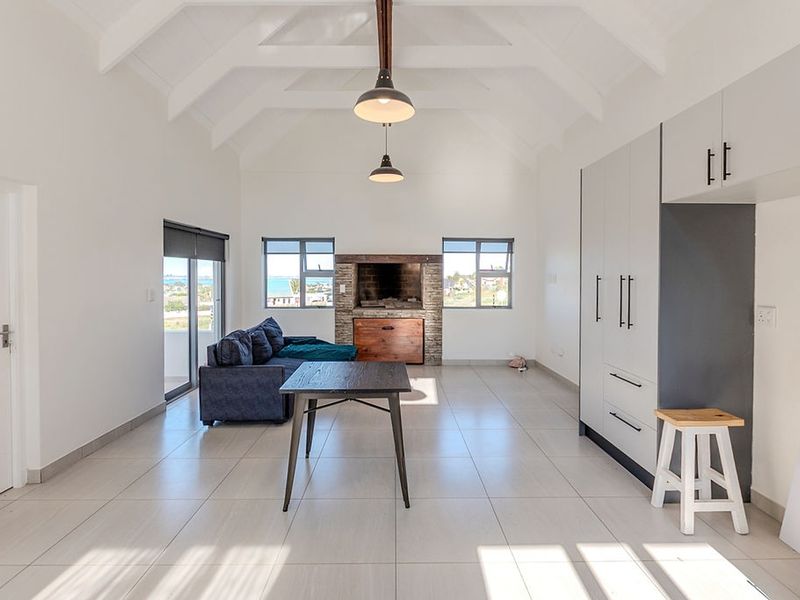 Spacious open-plan living area featuring a vaulted ceiling with exposed rafters, tiled flooring, built-in fireplace, and modern cabinetry with direct access to outdoor space.
