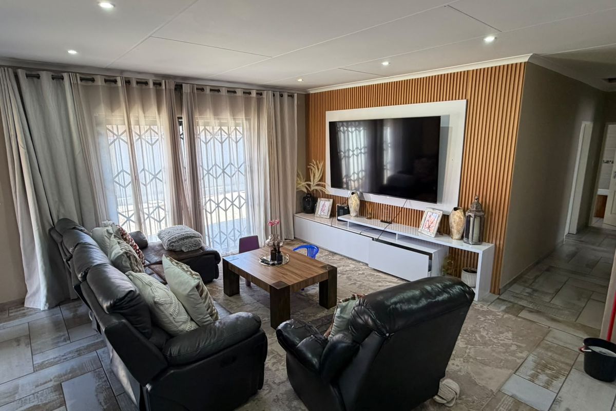A modern living room featuring a slatted timber accent wall, built-in media console, recessed lighting, and tiled flooring with access to the patio.