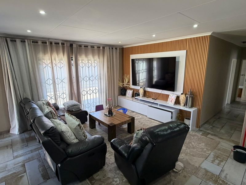 A modern living room featuring a slatted timber accent wall, built-in media console, recessed lighting, and tiled flooring with access to the patio.