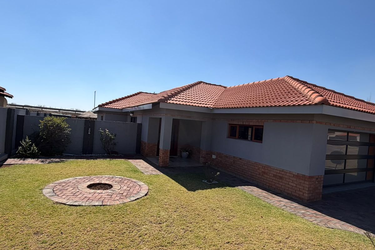 A well-maintained rear exterior view featuring a brick and plaster facade, terracotta tiled roof, paved driveway, and a circular brick fire pit in the garden.