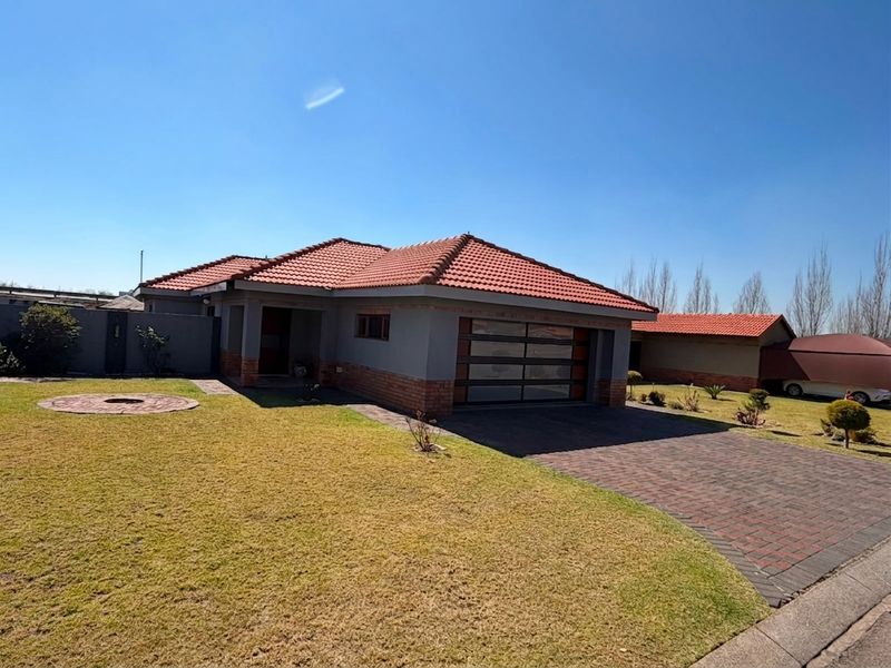 Front elevation of a single-story house featuring a tiled roof, brick driveway, and a modern sectional garage door with a well-maintained lawn.