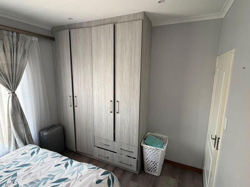 A well-maintained bedroom featuring light wood-grain built-in cupboards, recessed ceiling lighting, and modern laminate flooring.