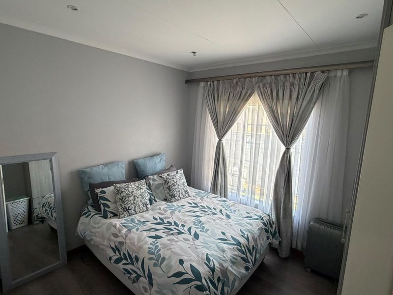 A well-maintained bedroom featuring laminate flooring, recessed downlighting, and a large window dressed with curtains.