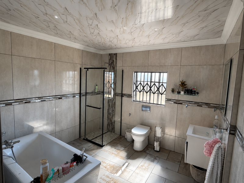 Modern bathroom featuring a bathtub, glass-enclosed shower, wall-mounted toilet, and vanity basin with neutral floor-to-ceiling tiling and decorative ceiling finish.