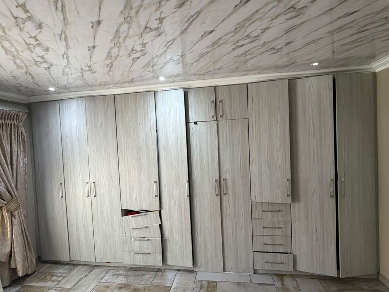 Bedroom featuring extensive built-in cabinetry with wood-grain finish, recessed lighting, and tiled flooring. Note that some cupboard doors and drawers require repair.