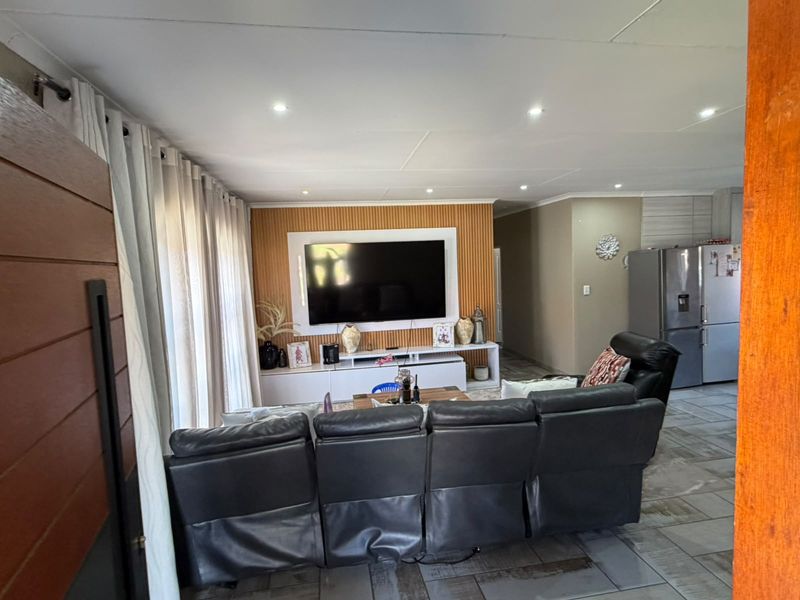 Open plan living area featuring tiled flooring, recessed downlighting, and a modern feature wall with a built-in media unit.