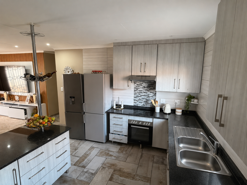 Modern kitchen featuring light wood-grain cabinetry, dark granite countertops, stainless steel appliances, and a functional island layout with tiled flooring.