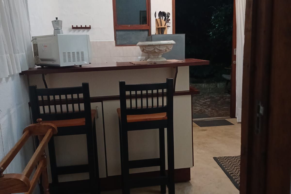 A compact kitchen area featuring a breakfast bar, tiled backsplash, and direct access to the exterior through a timber-framed door.