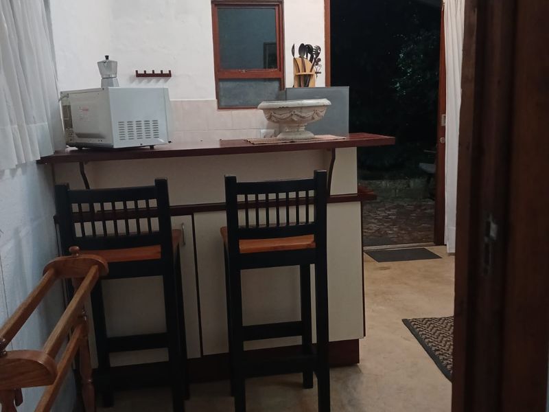 A compact kitchen area featuring a breakfast bar, tiled backsplash, and direct access to the exterior through a timber-framed door.