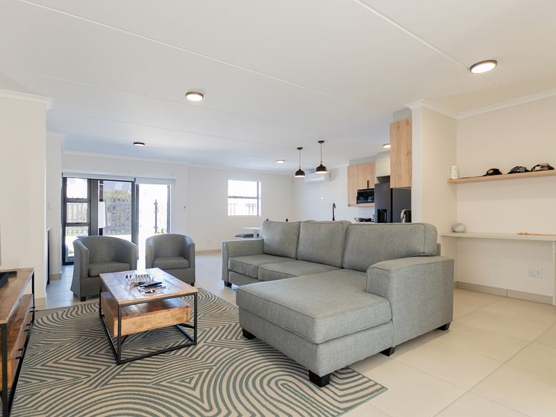 A bright open-plan living and kitchen area featuring modern tiled floors, recessed lighting, and a functional kitchen layout with built-in cabinetry.