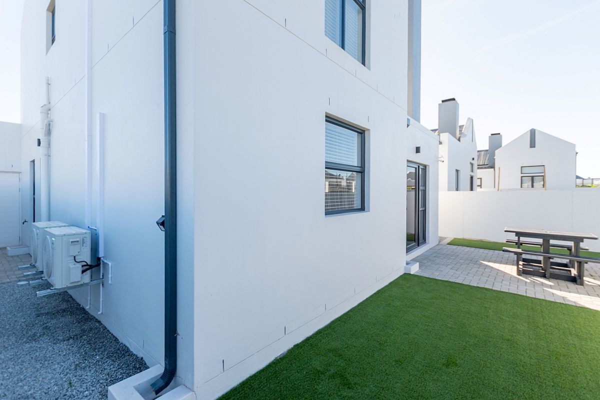 Rear exterior view of the property featuring a paved patio area, artificial lawn, and wall-mounted air conditioning units.