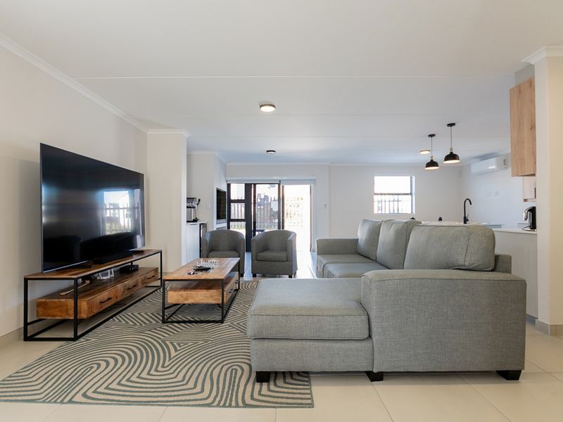Spacious open-plan living area featuring tiled floors, recessed lighting, and a seamless flow into the modern kitchen space with direct access to the outdoors.