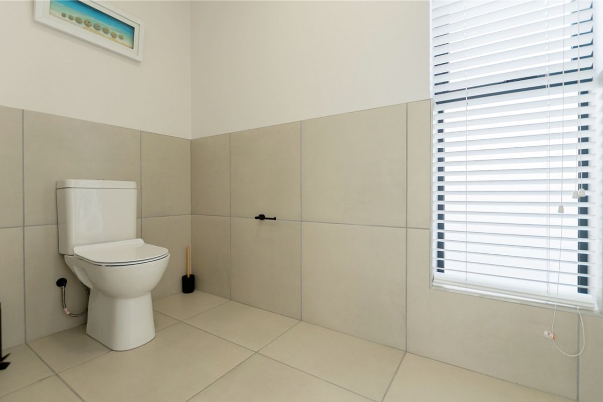 A clean, minimalist bathroom featuring neutral large-format wall and floor tiles, a modern toilet, and fitted venetian blinds.