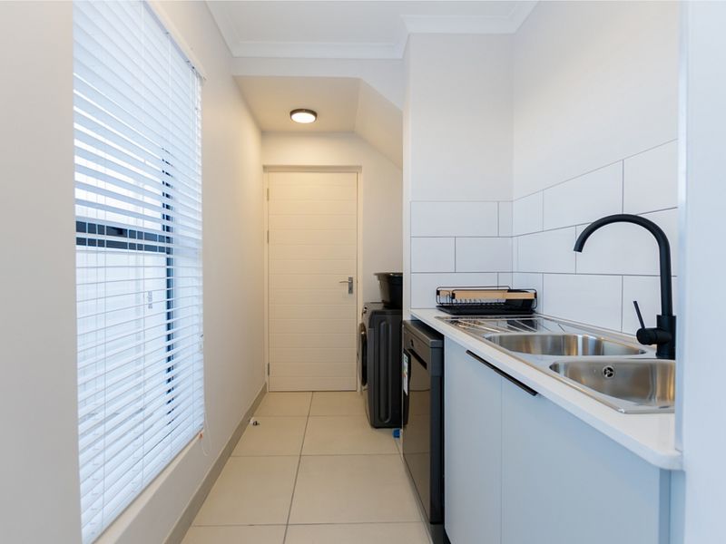 Modern laundry area featuring a stainless steel sink, matte black tapware, subway tile splashback, and clean tiled flooring.
