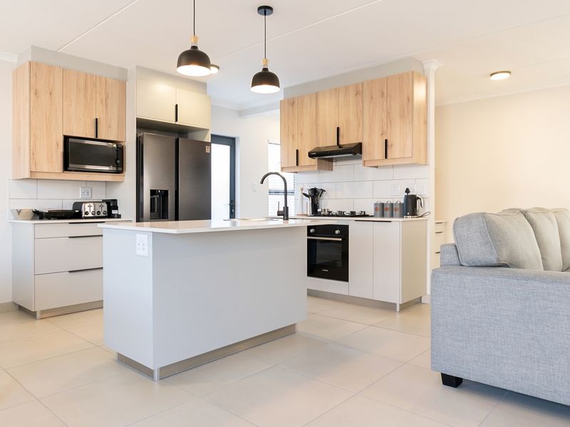Modern open-plan kitchen featuring light wood and white cabinetry, a central island, built-in appliances, and sleek tiled flooring.