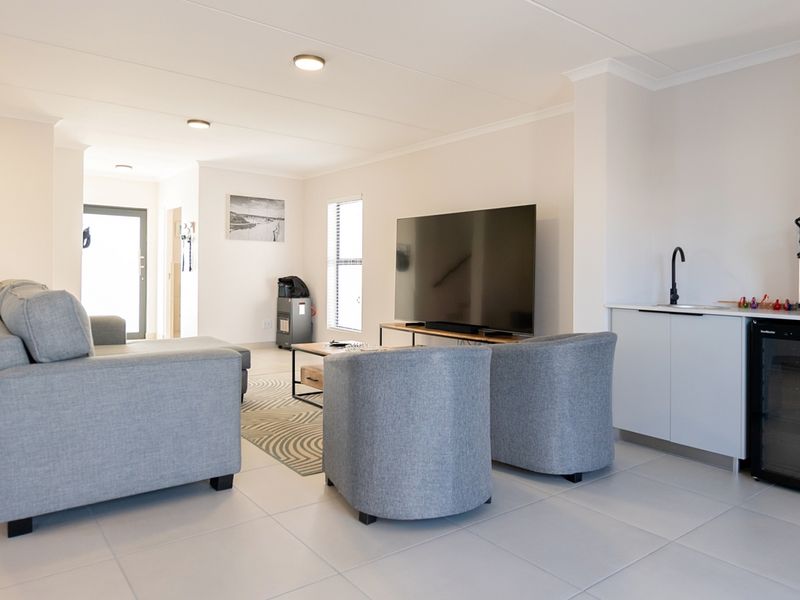 A bright open-plan living area featuring tiled flooring, recessed lighting, and a convenient built-in kitchenette unit with a sink.