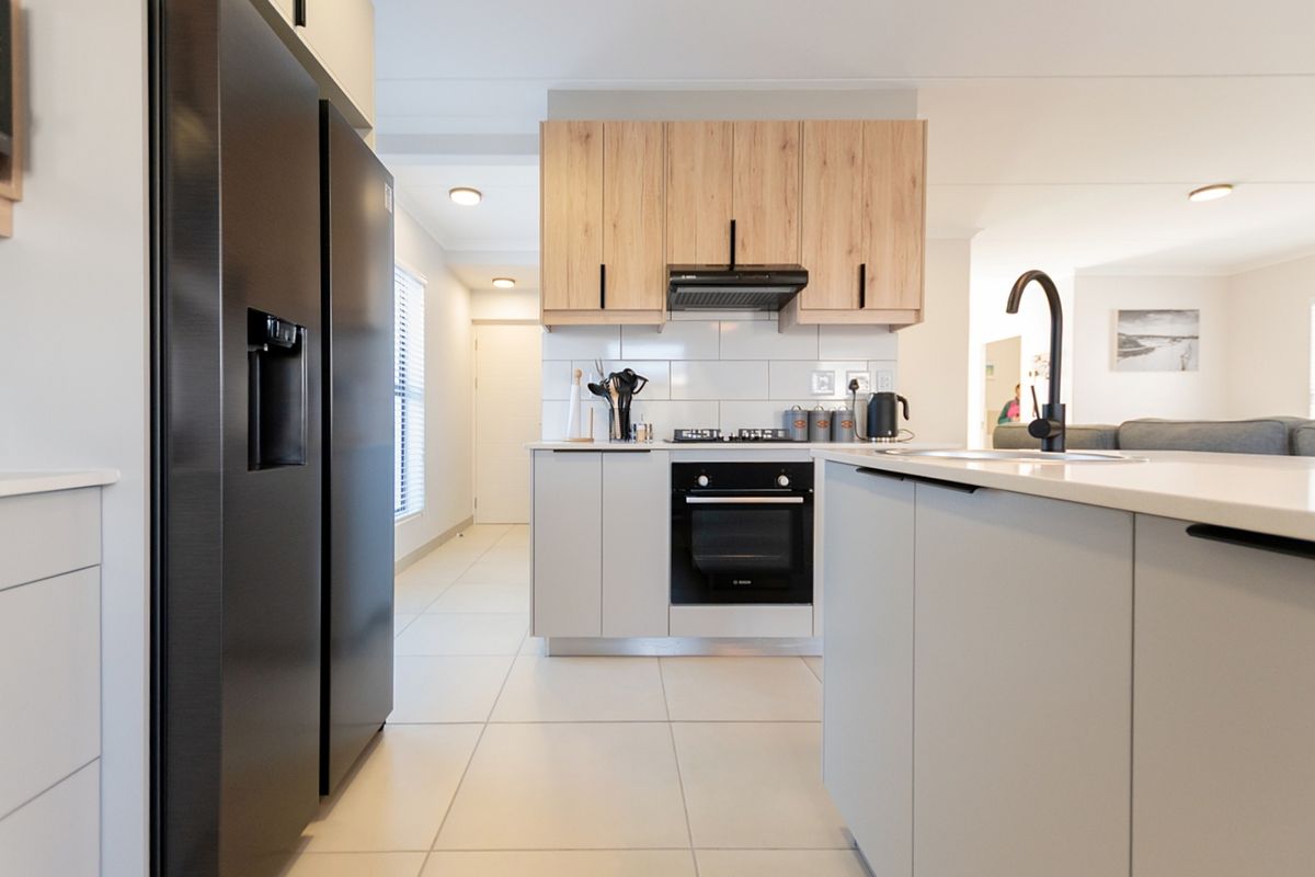 Modern kitchen featuring light wood and grey cabinetry, subway tile backsplash, built-in oven, gas hob, and a functional island with a sink.
