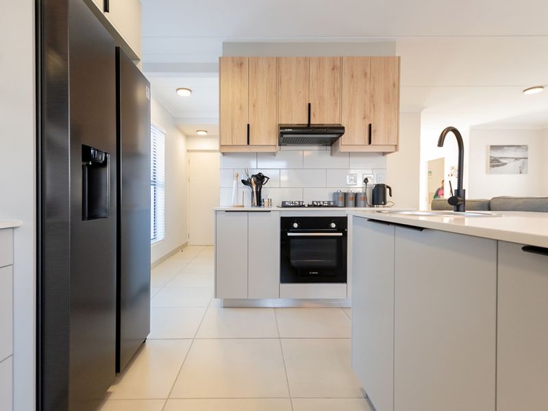 Modern kitchen featuring light wood and grey cabinetry, subway tile backsplash, built-in oven, gas hob, and a functional island with a sink.