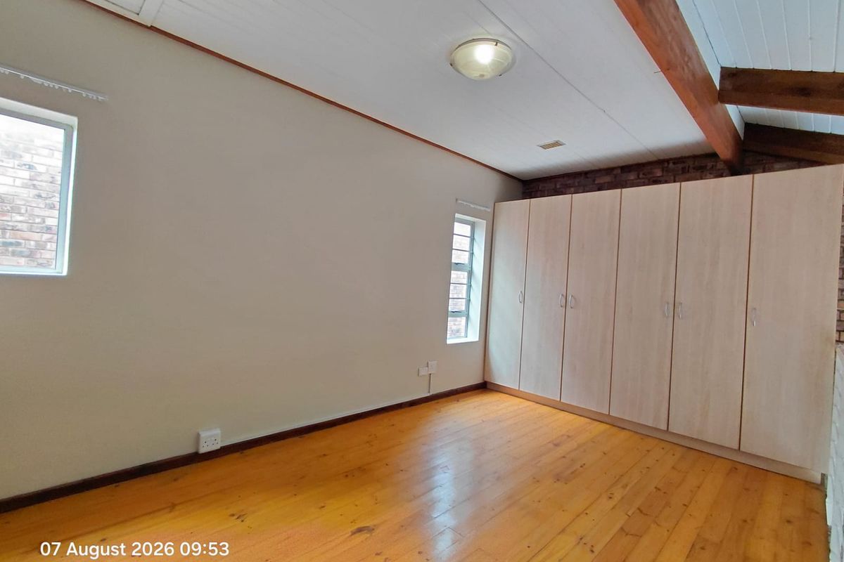 A spacious bedroom featuring polished timber flooring, exposed timber ceiling beams, exposed brick accents, and extensive built-in cupboard storage.