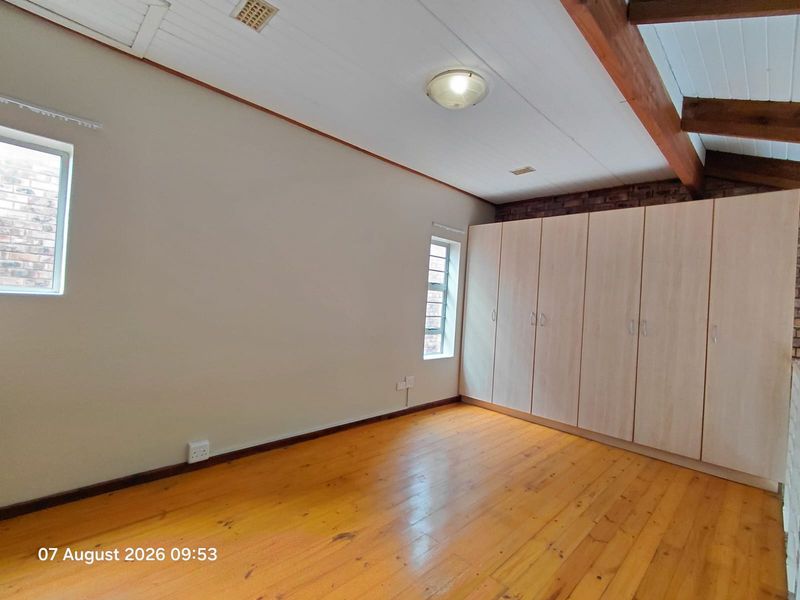 A spacious bedroom featuring polished timber flooring, exposed timber ceiling beams, exposed brick accents, and extensive built-in cupboard storage.