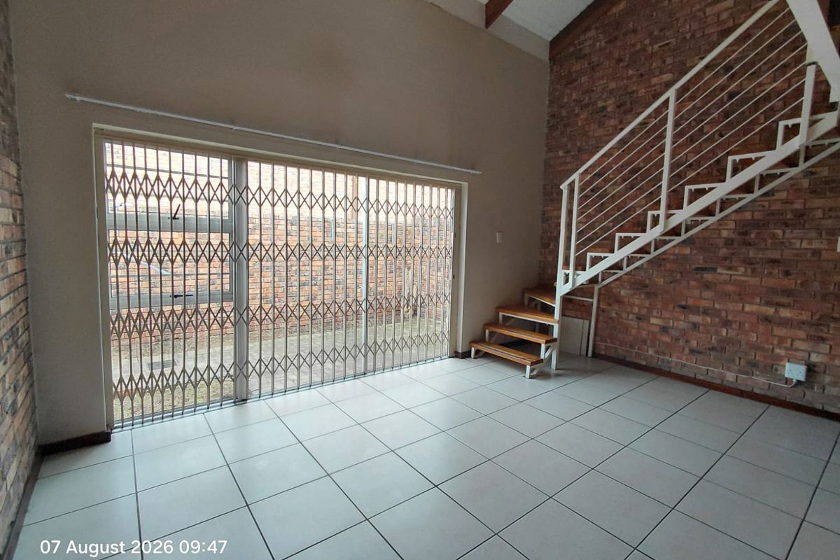 Spacious living area featuring exposed brick walls, tiled flooring, and a modern metal staircase leading to the upper level.